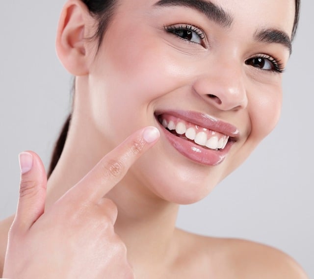 Close-up of a smiling woman pointing at her full, hydrated lips after a dermatology exam.